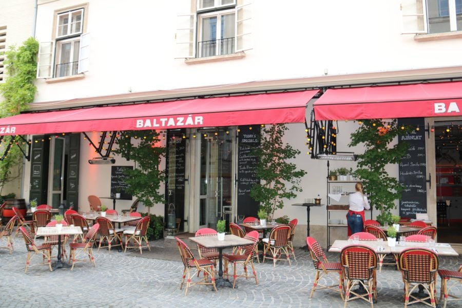 exterior of Balthazar Hungarian restaurant Budapest with red awning over patio tables with red chairs