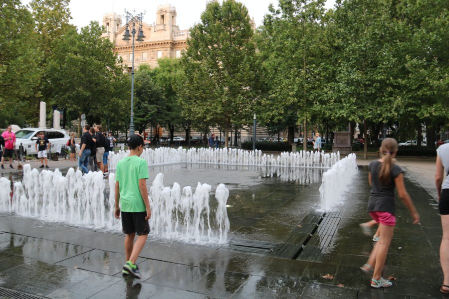 image of a square in ground fountain with Caiden walking towards it