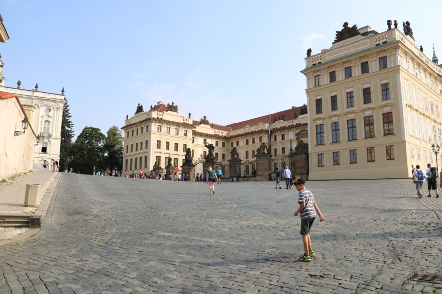 image of caiden walking through cobble stone square with palace buildings behind