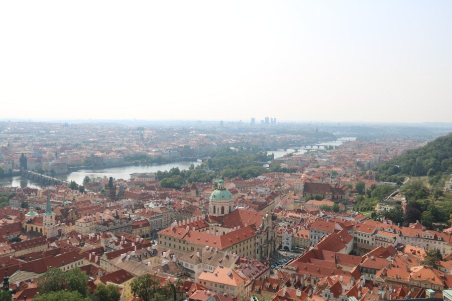 image from top of tower with orange rooftops and bridge in distance. Visiting is fun thing to do in Prague