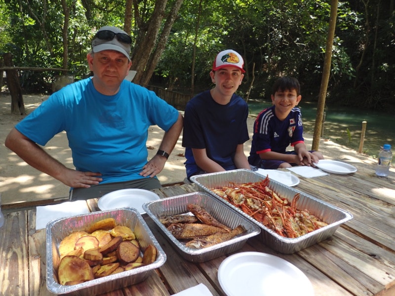 The boys sitting at picnic table with foil trays of plantain, fish and lobster