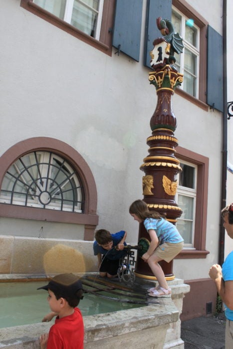 three kids getting drink from top of stone fountain