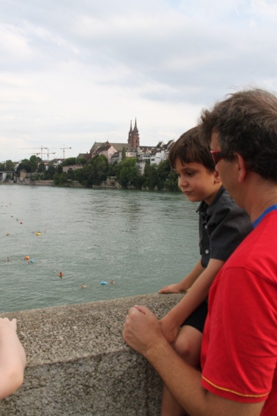 John and Caiden looking over the Mittlere Brücke to the Rhine and swimmers and Basel Munster 