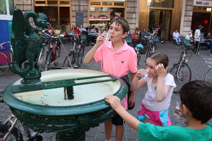 image of three kids drinking water from green basilisk fountain with plastic cups