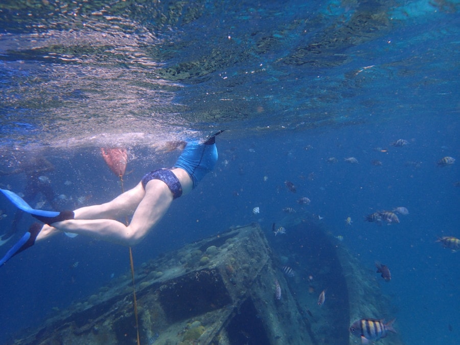 girl with blue bathing suit swimming above greenish shipwreck in blue water from Barbados catamaran excursion