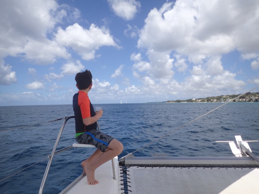 boy with orange tshirt sitting on front of Barbados catamaran enjoying wind