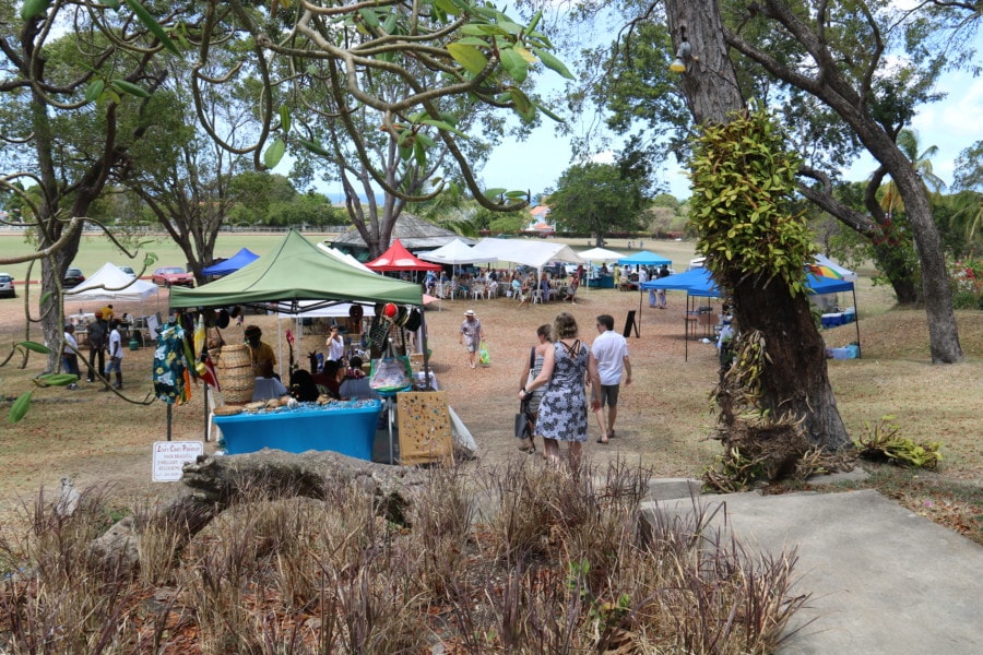 slight hill before field filled with covered tables is at Sunday market in Barbados