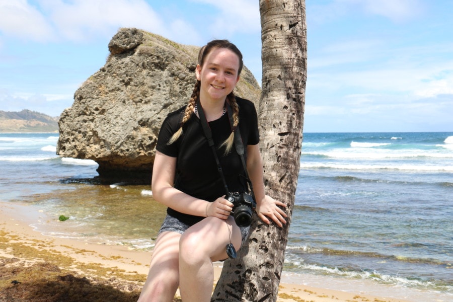 Sydney leaning on palm tree with large rock behind her