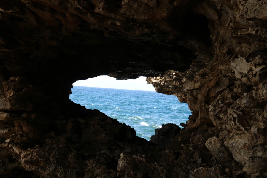 hole from inside cave looking out at blue sea with white caps
