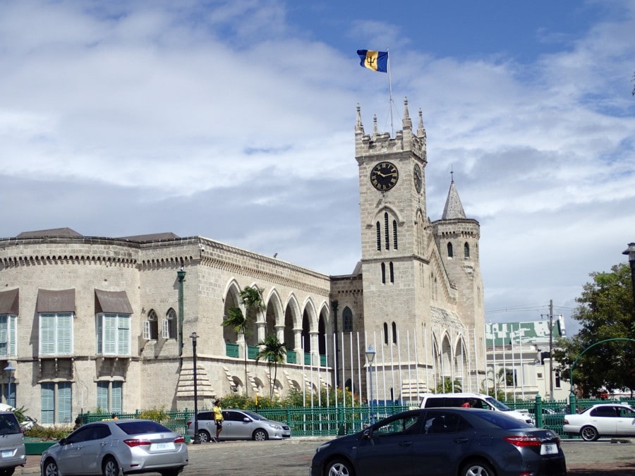 picture of Barbados parliament with large stone building with tall square tower and Barbados blue and gold flag flying