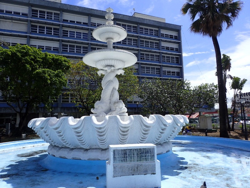 white fountain with shell on bottom and two dolphines holding two plates above is Barbados attraction in Bridgetown