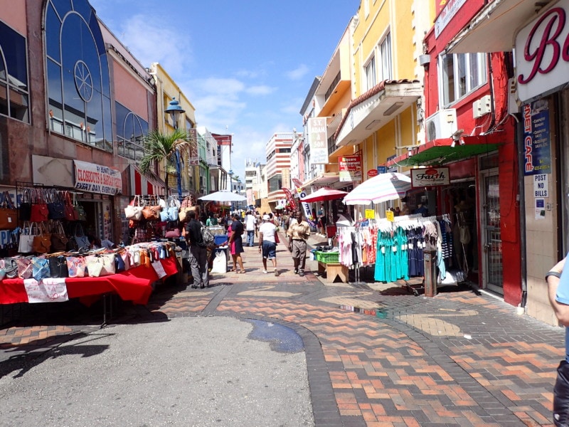 looking down cobblestone street with stores on each side and products like dresses outside shops is Barbados Attraction in Bridgetown