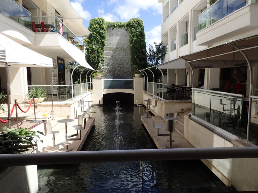 waterfall wall with greenery on each side and small rectangle lake below with shops on each side of lake at Limegrove shopping centre makes this a great Barbados attraction in Holetown