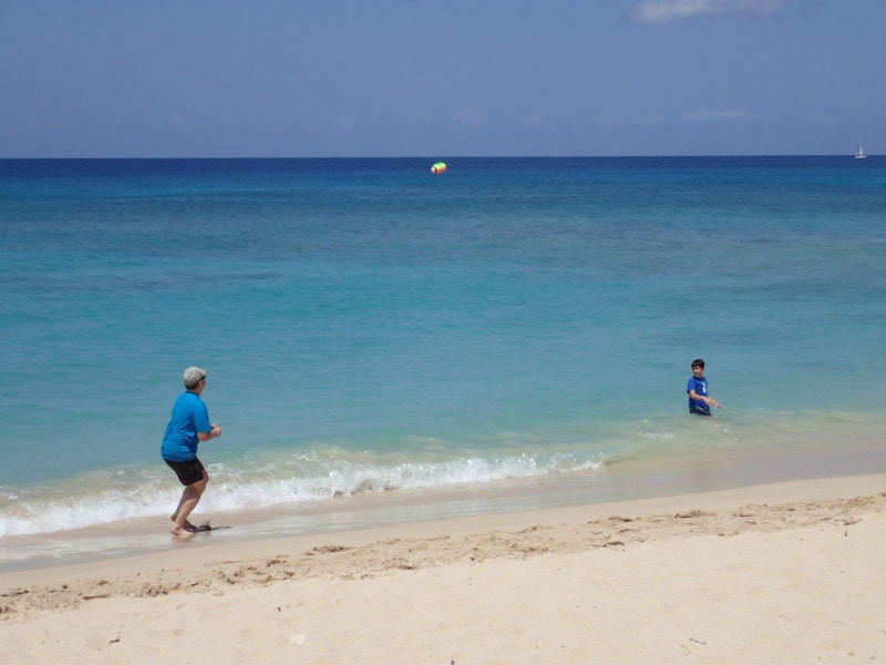 son and dad tossing football on beach at water edge Barbados Things to do