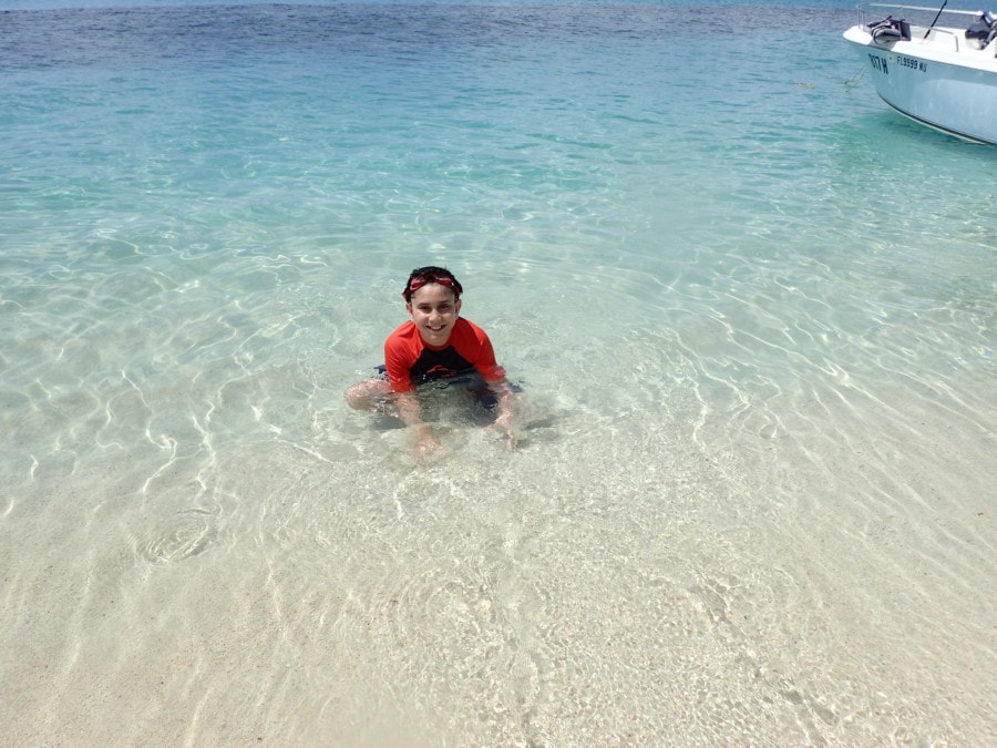 Boy with orange and blue shirt sitting in the water beside the beach