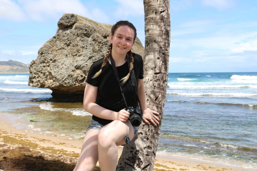 Girl leaning on palm tree with massive mushroom rock behind 