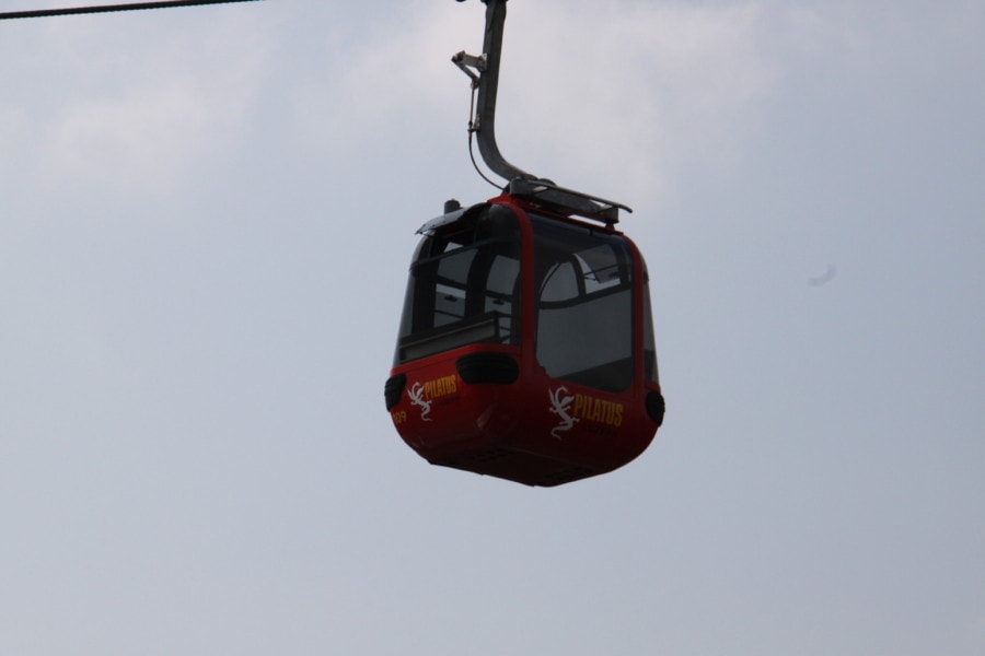 small red gondola enclosed with windows with yellow dragon and Mount Pilatus on outside