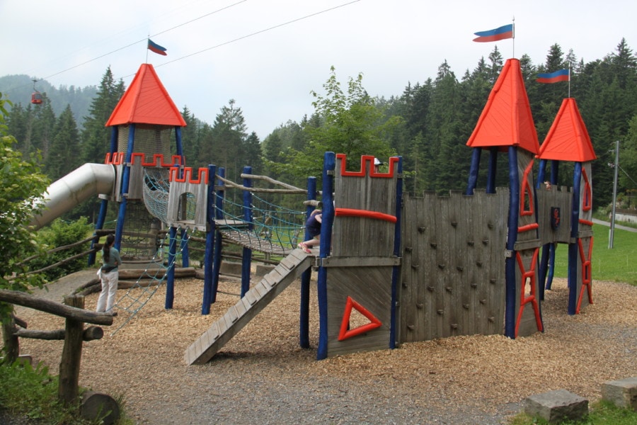 playground with ropes between landing pads with orange peaked roofs that makes it look like castles with climbing wall and rope