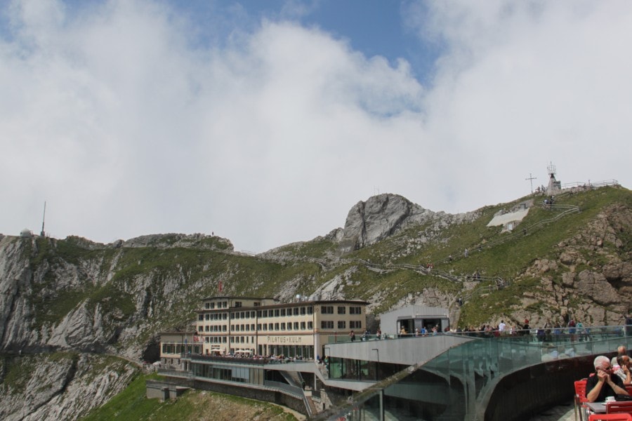 distant view of beige hotel with part of Mount Pilatus behind and stairs with railing going to the top