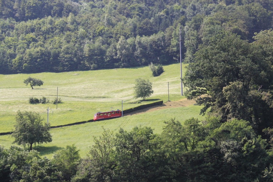 red cogwheel train in distance climbing back up lower green part of Mount Pilatus