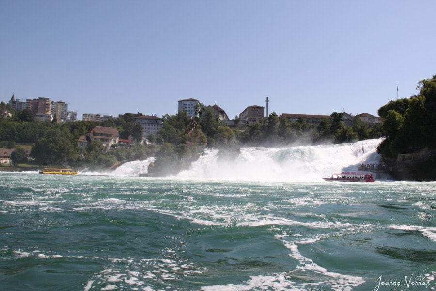 view from the boat of wide Rheinfall crashing around large rock with people on top