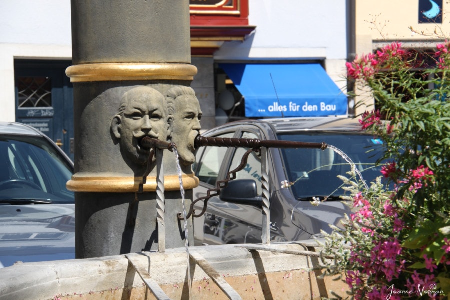 the base of Platz fountain with several faces with pipes and water coming from them