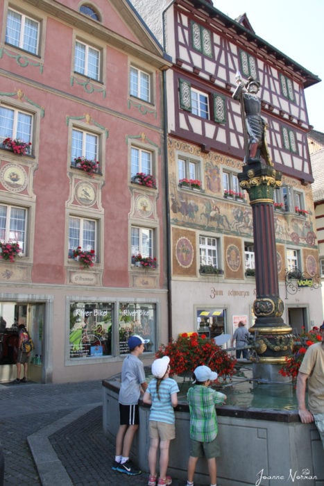 fountain with tall statue on tope in gold and green with painted houses behind in Stein am Rhein old town