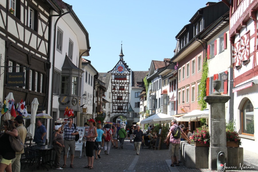 Main gate to Stein am Rhein and the cobblestone street with traditional painted tall joined houses on each side and clock tower and main gates at end of street