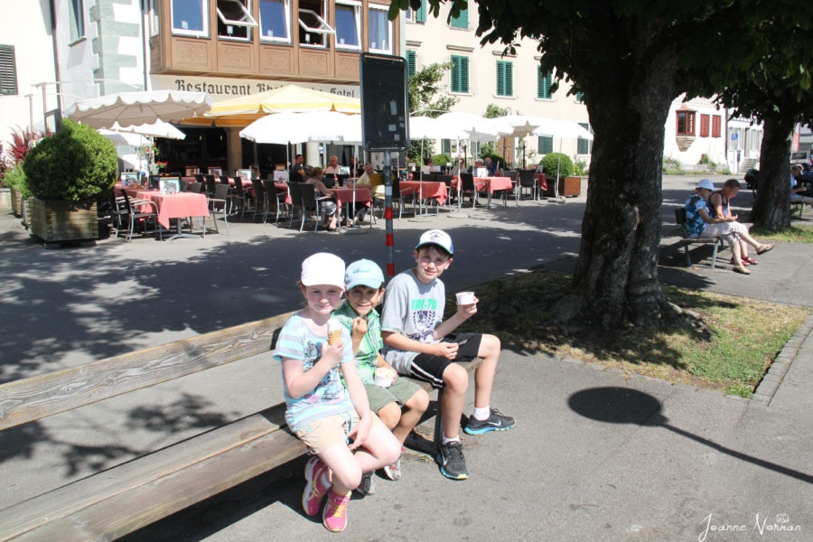 three kids sitting on a bench eating ice cream
