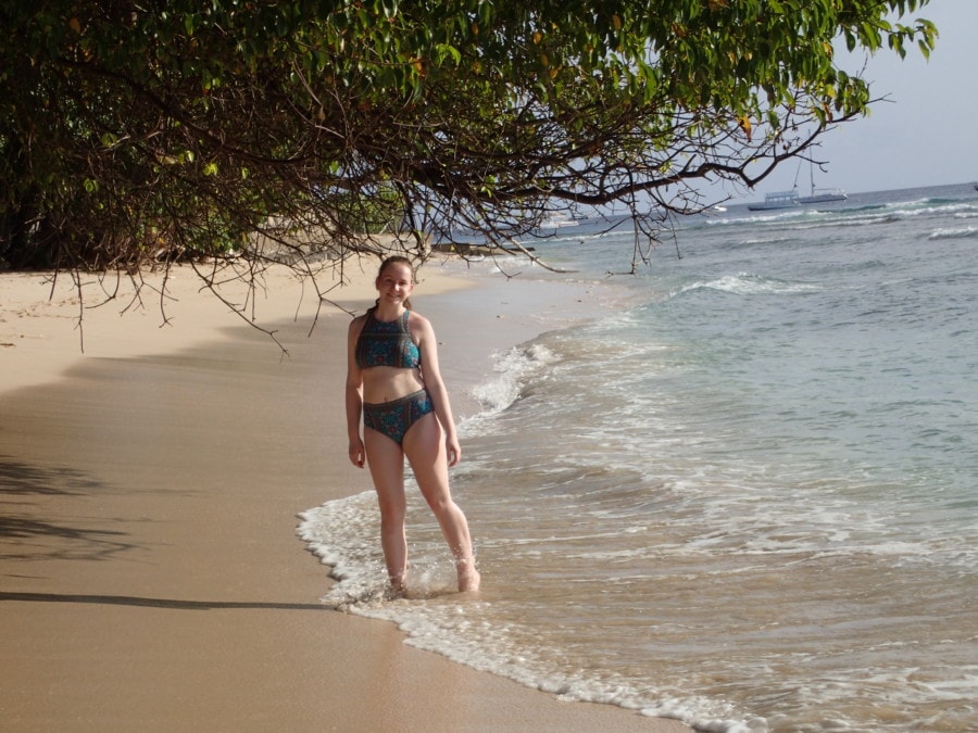 girl in green bathing suit standing under tree on beach