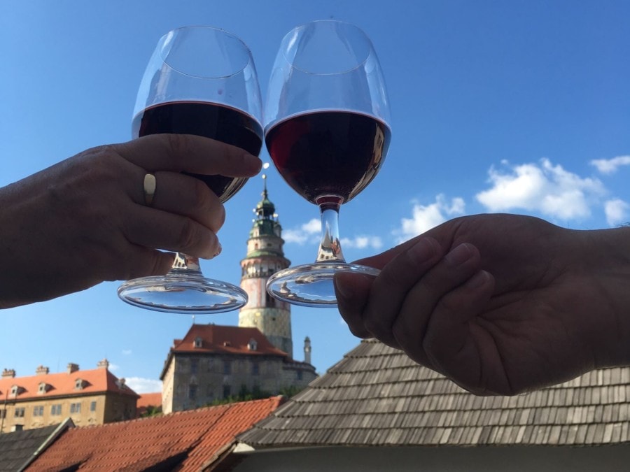 two wine glasses clinking together with Krumlov castle tower in between in the distance