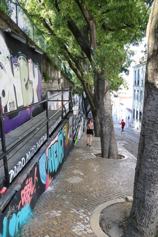 cobblestone sidewalk with trees and wall filled with graffiti for for Lisbon with kids