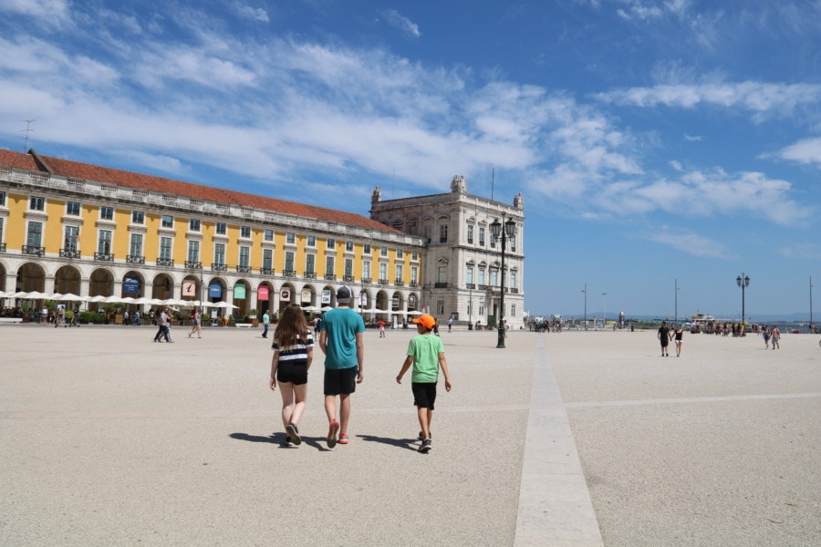 My three kids walking across open square with yellow building along side is Praca Comercio