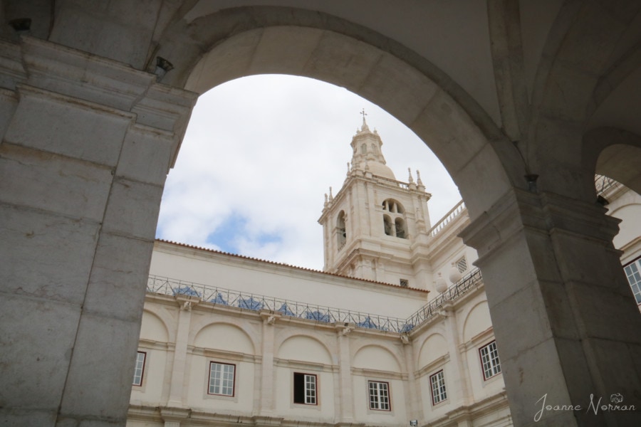 photo taken through white stone archway of steeple of Monastery in Alfama Lisbon