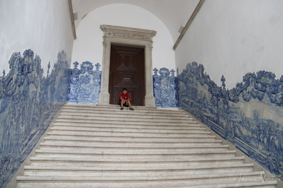 white marble stairs with blue tiles on walls and kid in red shirt in front of brown wooden door 