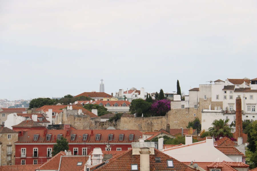 view of orange roof tops with Christo statue in distance in Alfama Lisbon with kids