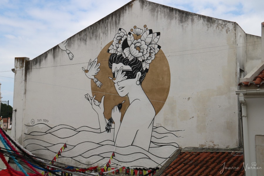 black and white street art of lady with flowers on her head and birds in her hands