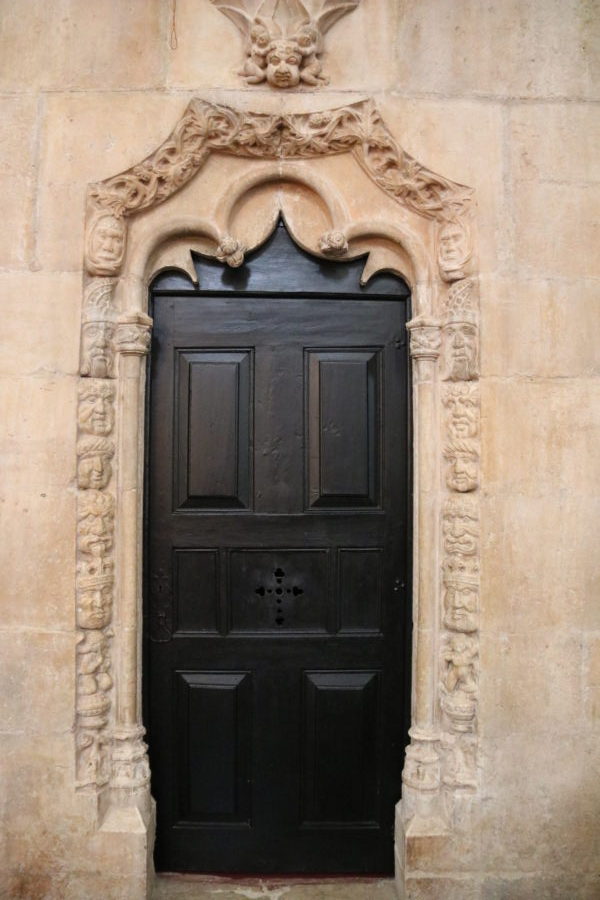 black wooden door with decorative stone trim showing faces during a day in Belem
