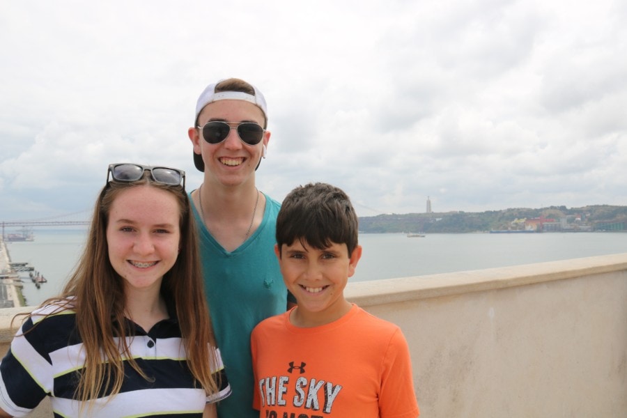 two boys and one girl standing on top of monument with Christ statue in background