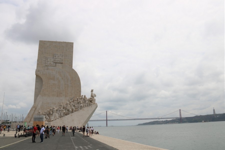 distant view of monument as sailboat with explorers carved into side as viewed from further down waterfront walkway