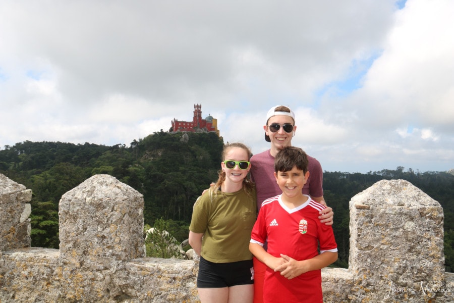 three teens standing on castle wall with view of red palace behind them Lisbon to Sintra