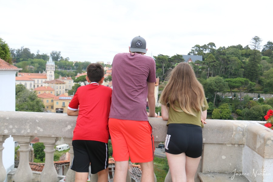 three kids leaning on stone railing looking over village