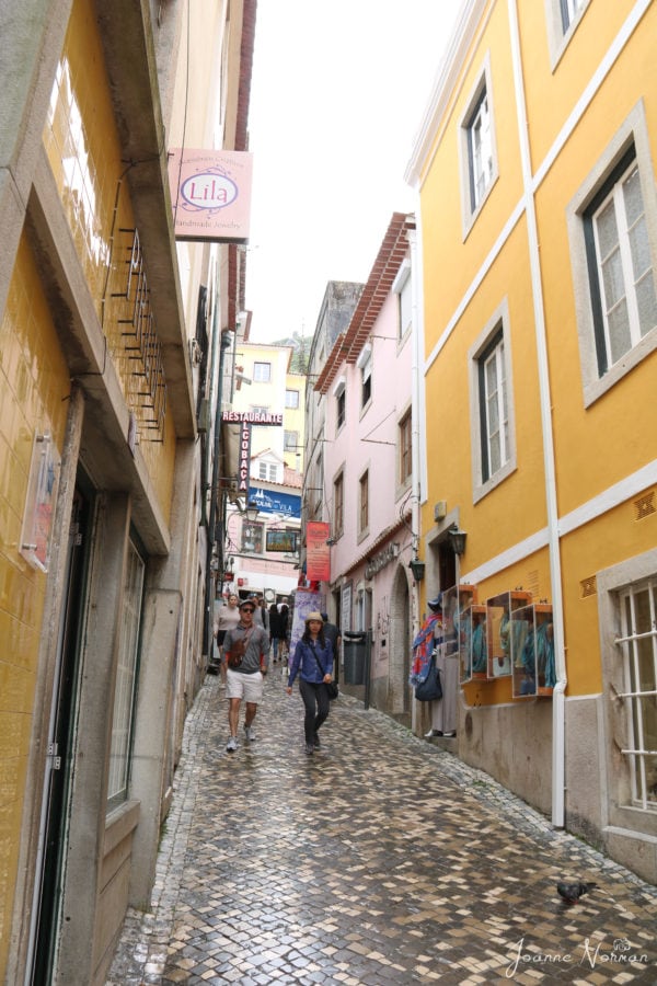 inclined cobblestone street with yellow and pink houses on each side