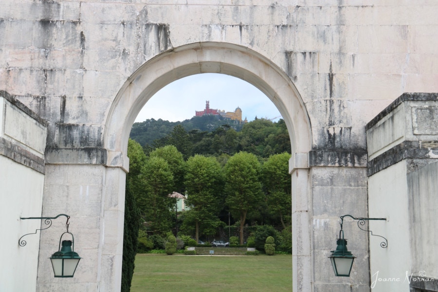 looking through archway with antique lights hanging on side to see pena palace on top of green hill in distance on daytrip from lisbon