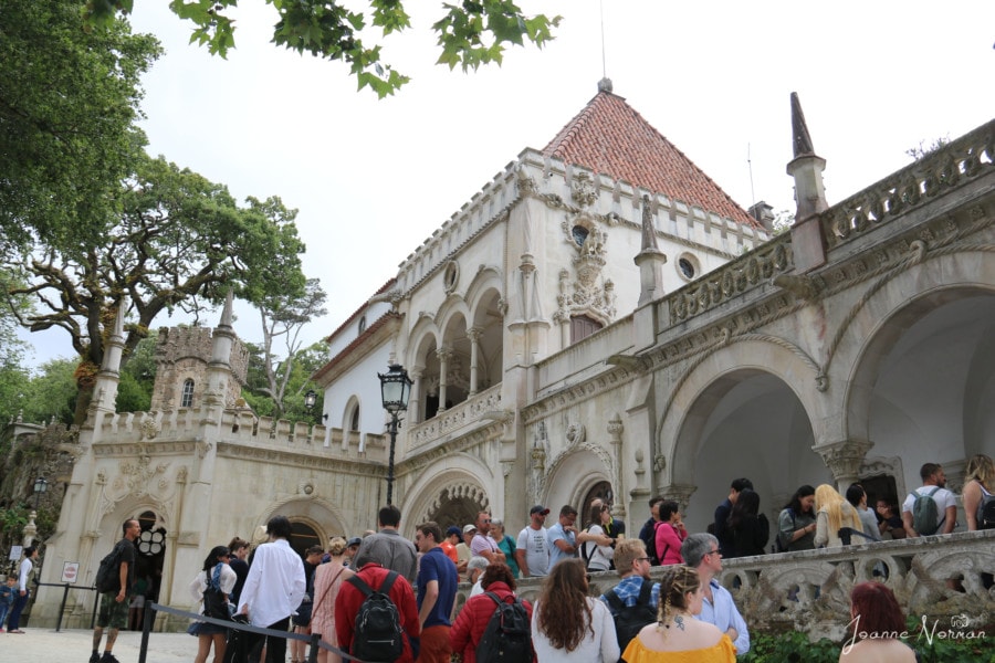 entrance building to Quinta da Regaleira showing stone building with arches and orange roof and long line of people