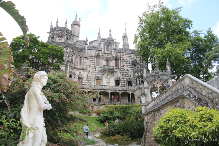 outside of palace with many peaks and bridge and white statue leading to it