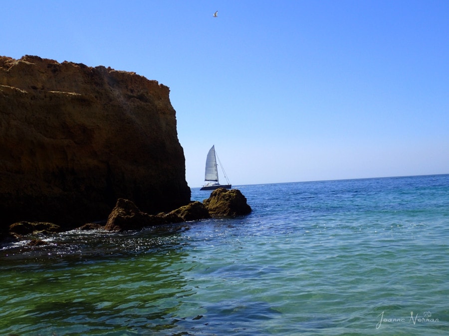cliffs next to water with white sailboat passing in Carvoeiro Portugal