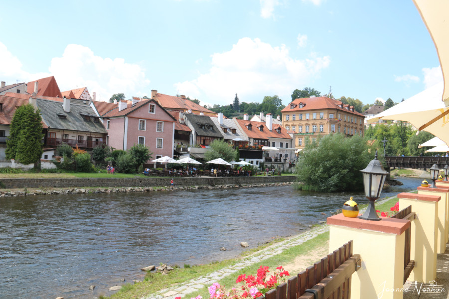 small river lined with red flowers and houses with orange roofs is cesky krumlov