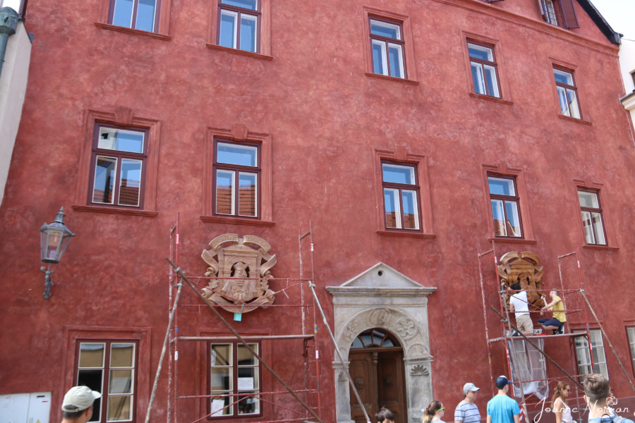 red building with two crests in front and workers painting one of them