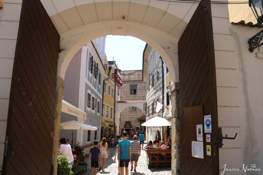 archway with wooden doors and narrow street beyond leads to castle